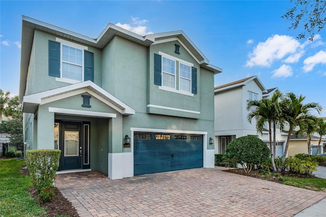 view of front of house with decorative driveway, an attached garage, and stucco siding