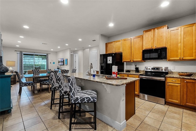 kitchen with light stone counters, recessed lighting, black appliances, an island with sink, and a kitchen breakfast bar