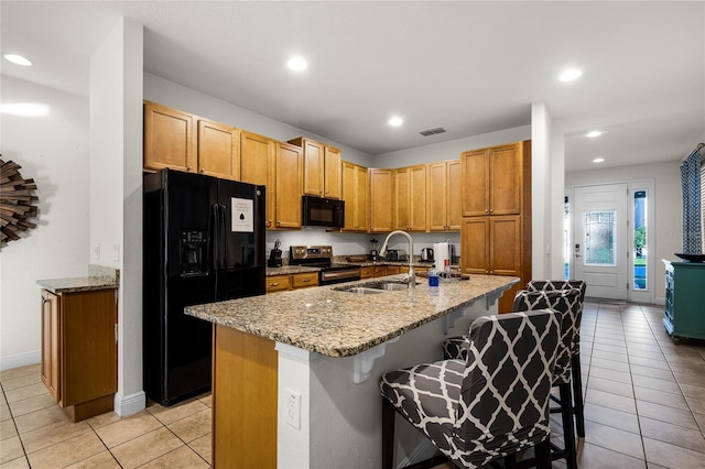 kitchen featuring an island with sink, black appliances, visible vents, and a sink