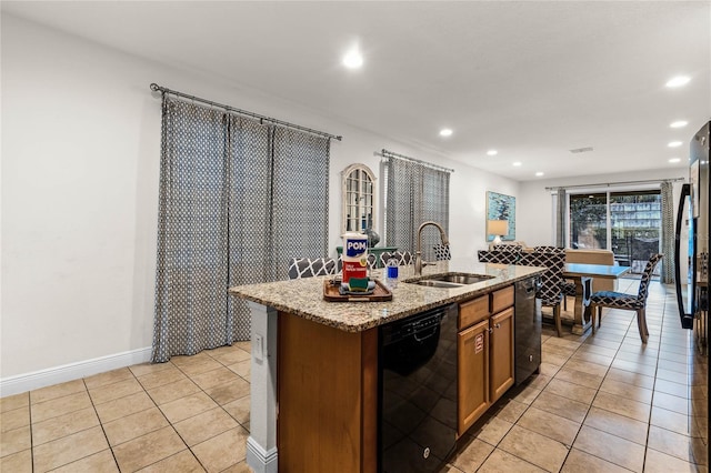 kitchen featuring brown cabinets, light tile patterned floors, a kitchen island with sink, a sink, and dishwasher