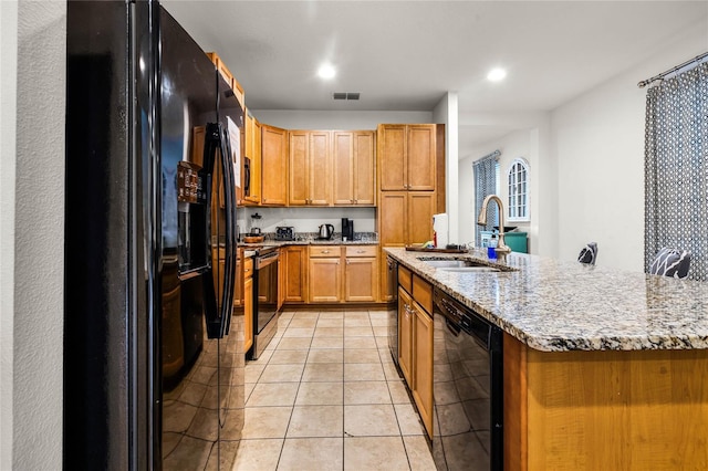 kitchen featuring a sink, visible vents, light stone countertops, black appliances, and a center island with sink