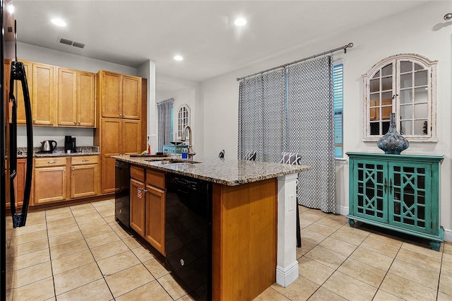 kitchen featuring light stone counters, light tile patterned floors, a kitchen island with sink, a sink, and dishwasher