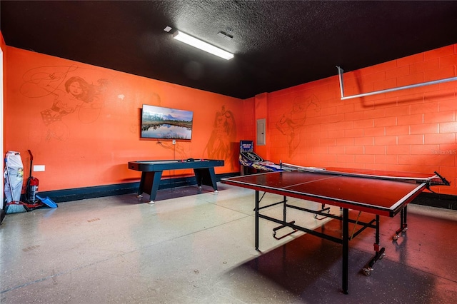 game room with concrete block wall, a textured ceiling, electric panel, baseboards, and speckled floor