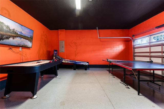 playroom featuring a garage, concrete block wall, electric panel, and light speckled floor