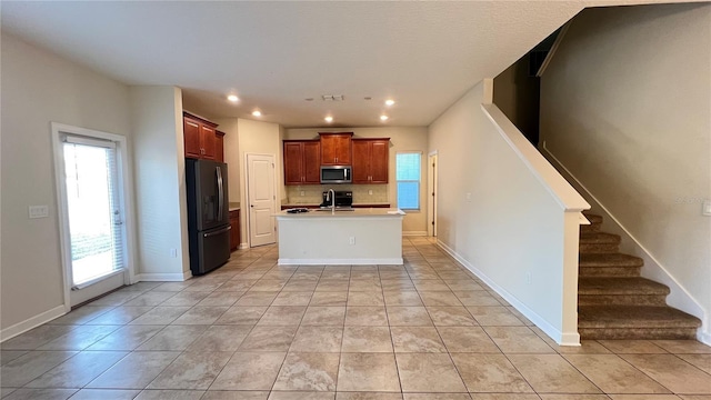 kitchen with black refrigerator, light tile patterned floors, a wealth of natural light, and an island with sink