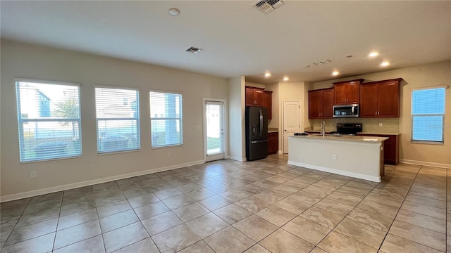 kitchen with range with electric stovetop, an island with sink, sink, black fridge with ice dispenser, and plenty of natural light