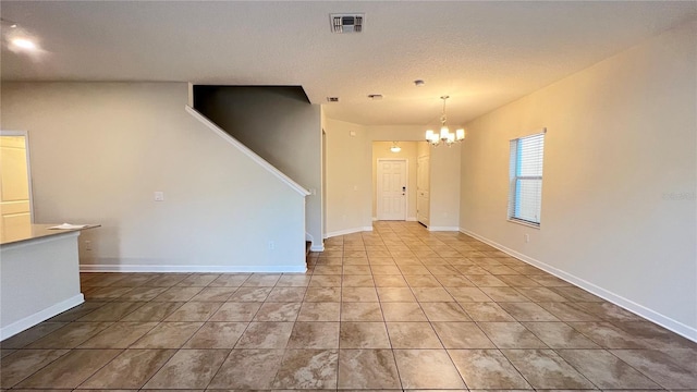 tiled empty room featuring a textured ceiling and a chandelier