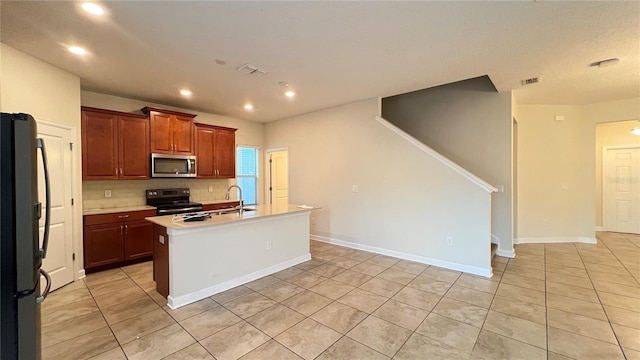 kitchen with appliances with stainless steel finishes, a center island with sink, backsplash, and light tile patterned floors