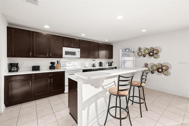 kitchen featuring a kitchen bar, dark brown cabinets, light tile patterned floors, a kitchen island, and white appliances