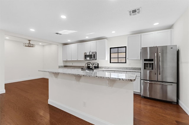 kitchen with appliances with stainless steel finishes, a kitchen island with sink, white cabinets, and a kitchen bar