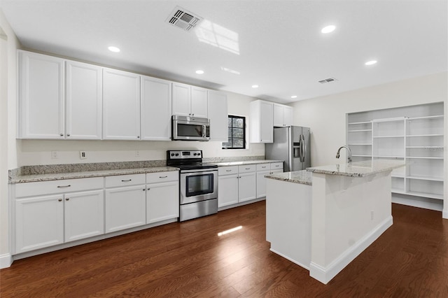 kitchen with stainless steel appliances, light stone countertops, an island with sink, and white cabinets