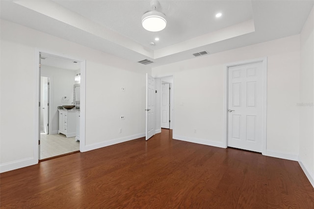 unfurnished bedroom featuring a raised ceiling and dark hardwood / wood-style flooring