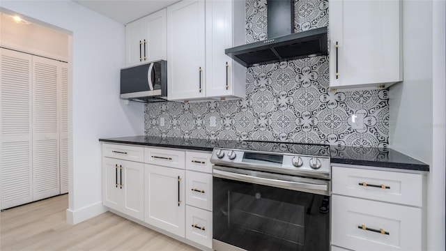 kitchen with appliances with stainless steel finishes, white cabinets, backsplash, wall chimney exhaust hood, and light hardwood / wood-style flooring