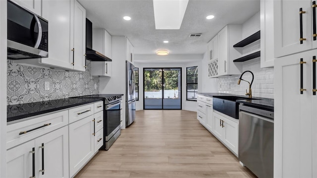 kitchen with wall chimney exhaust hood, sink, white cabinetry, light hardwood / wood-style flooring, and appliances with stainless steel finishes