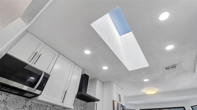 room details featuring white cabinetry, wall chimney exhaust hood, and a textured ceiling