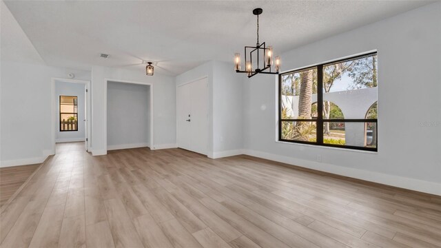 empty room with a textured ceiling, a wealth of natural light, a notable chandelier, and light hardwood / wood-style floors