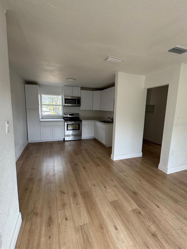 kitchen with sink, a textured ceiling, appliances with stainless steel finishes, light hardwood / wood-style floors, and white cabinets