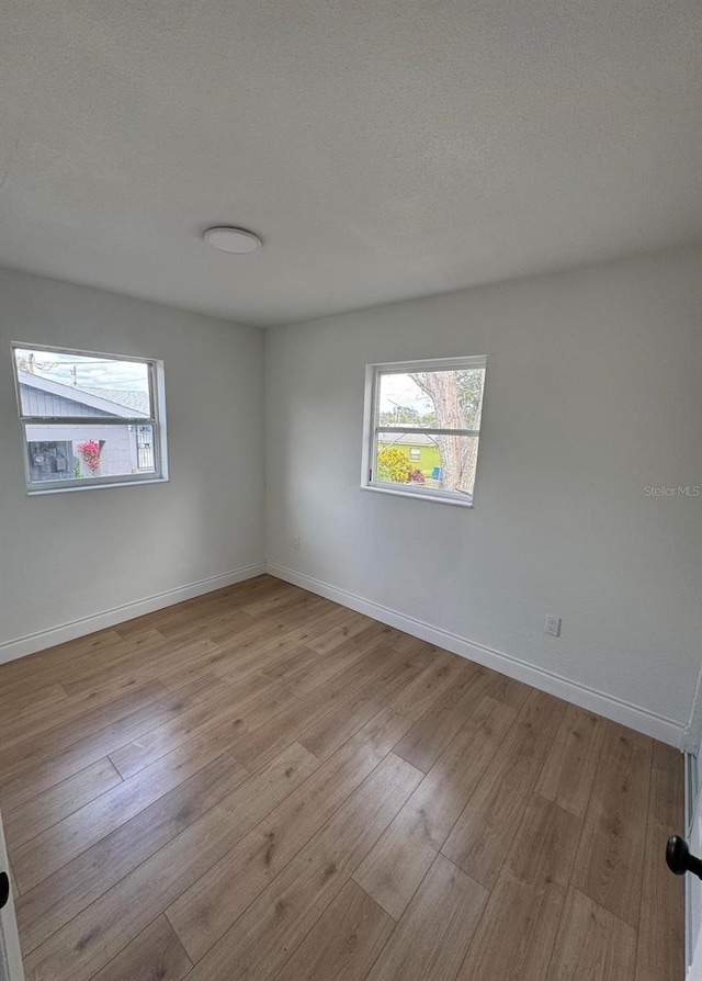 spare room with a healthy amount of sunlight, a textured ceiling, and light hardwood / wood-style floors