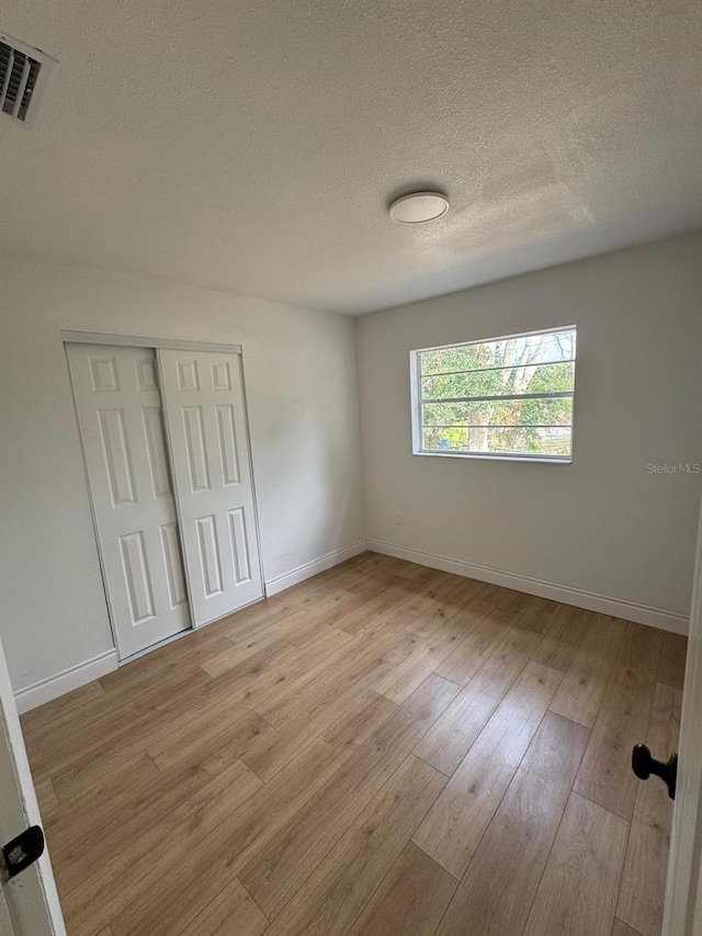 unfurnished room with light hardwood / wood-style flooring and a textured ceiling