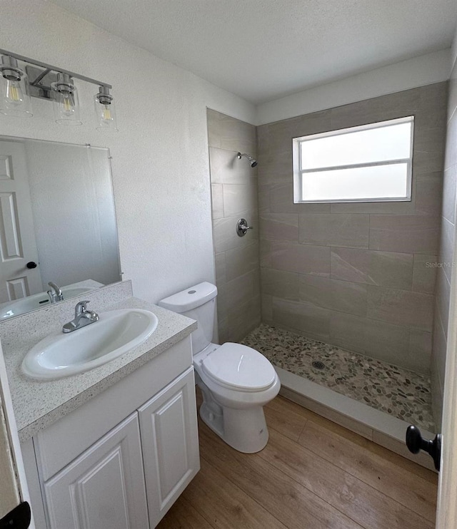 bathroom featuring hardwood / wood-style flooring, vanity, tiled shower, and toilet