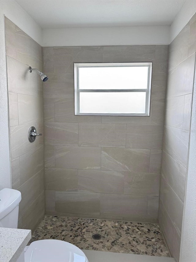 bathroom featuring vanity, a tile shower, and toilet