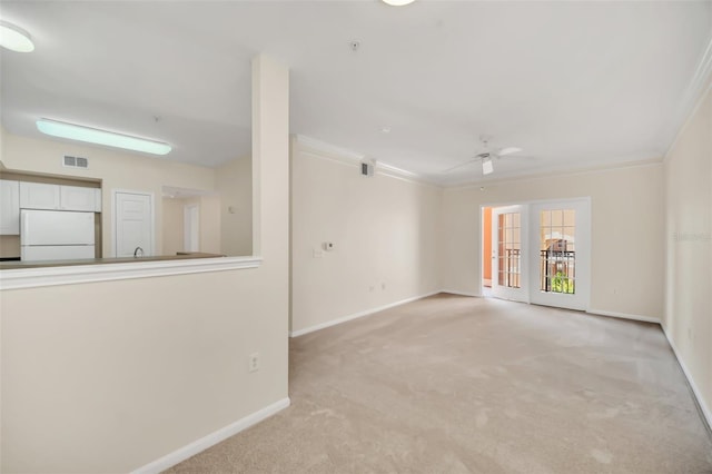 unfurnished living room with crown molding, light colored carpet, ceiling fan, and french doors