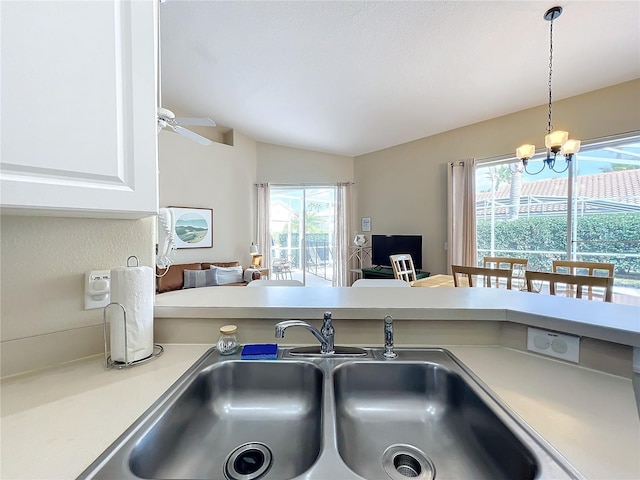 kitchen featuring lofted ceiling, sink, white cabinetry, pendant lighting, and ceiling fan with notable chandelier