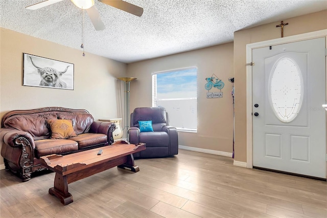 living room with ceiling fan, a textured ceiling, and light wood-type flooring