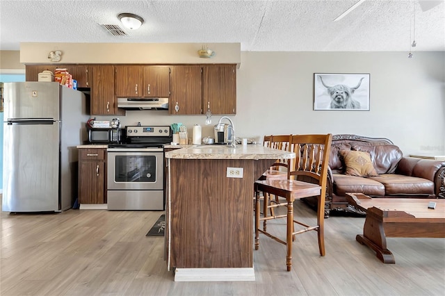 kitchen with sink, a kitchen breakfast bar, light hardwood / wood-style floors, stainless steel appliances, and a textured ceiling