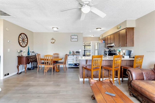 kitchen with light hardwood / wood-style flooring, a textured ceiling, appliances with stainless steel finishes, kitchen peninsula, and ceiling fan