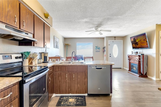 kitchen with sink, light wood-type flooring, kitchen peninsula, ceiling fan, and stainless steel appliances