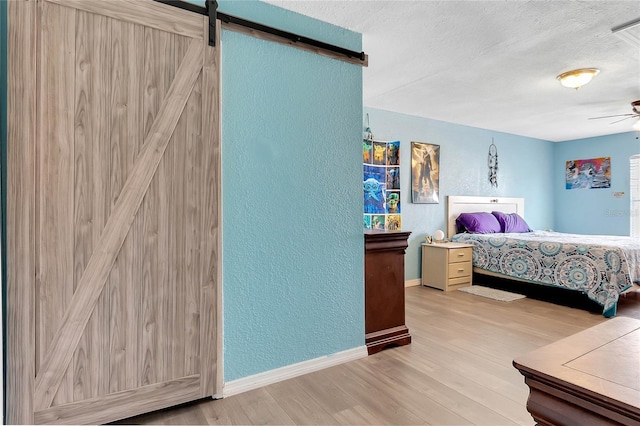 bedroom with a barn door, a textured ceiling, and light hardwood / wood-style floors