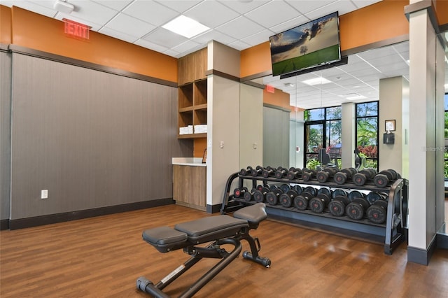 gym with dark hardwood / wood-style floors, a paneled ceiling, and a wall of windows