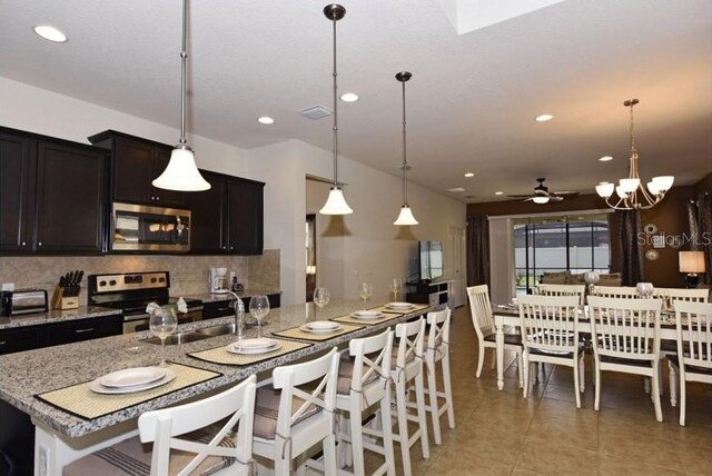 kitchen featuring sink, light tile patterned floors, appliances with stainless steel finishes, backsplash, and decorative light fixtures