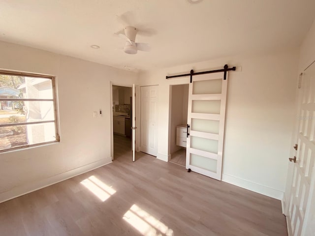 unfurnished bedroom featuring wood-type flooring, a barn door, and ceiling fan