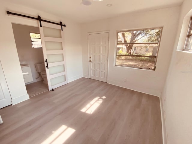 unfurnished bedroom with a closet, wood-type flooring, a barn door, and ensuite bathroom