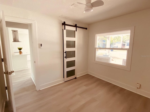 unfurnished bedroom featuring a barn door, a textured ceiling, and light wood-type flooring