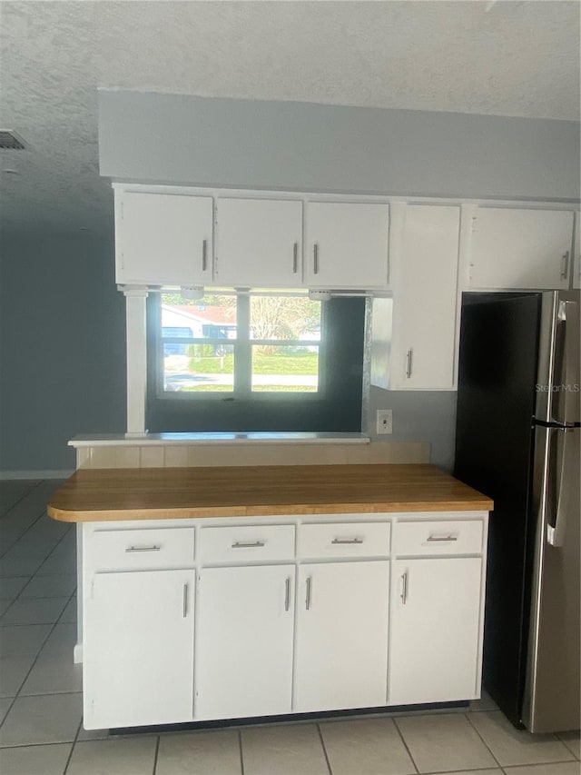 kitchen featuring white cabinetry, a textured ceiling, light tile patterned floors, stainless steel fridge, and kitchen peninsula