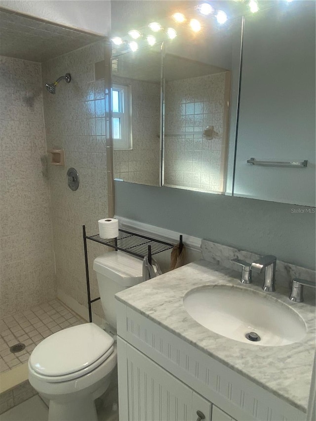 bathroom with a tile shower, vanity, and toilet