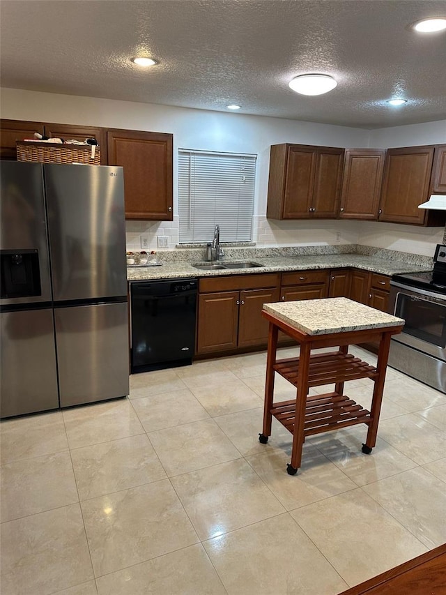 kitchen with sink, appliances with stainless steel finishes, light stone counters, a textured ceiling, and light tile patterned flooring