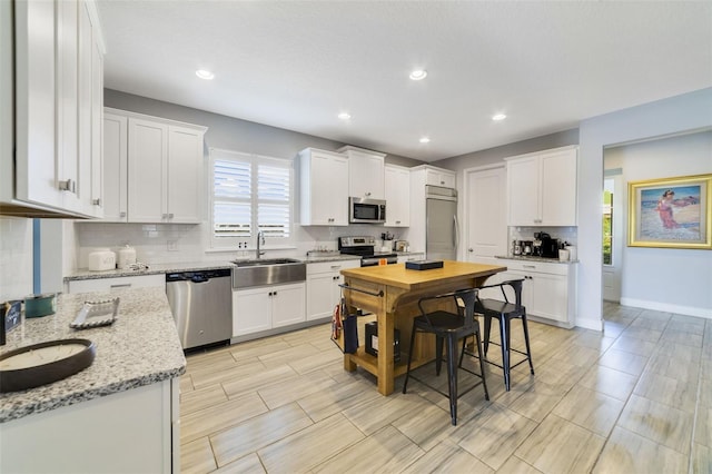 kitchen featuring sink, white cabinetry, stainless steel appliances, light stone countertops, and decorative backsplash