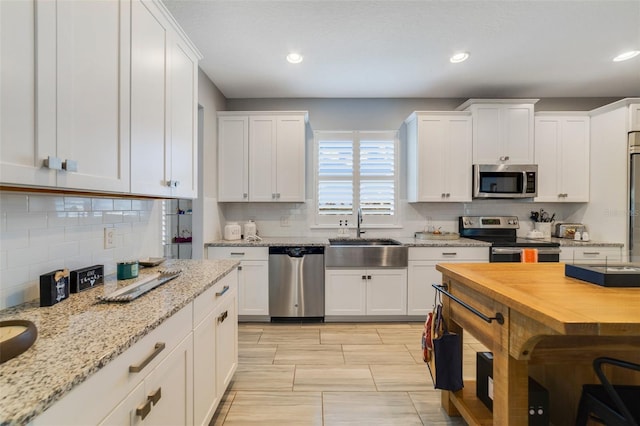 kitchen featuring white cabinetry, sink, backsplash, stainless steel appliances, and light stone countertops