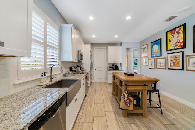 kitchen with white cabinetry, sink, backsplash, light stone counters, and stainless steel appliances