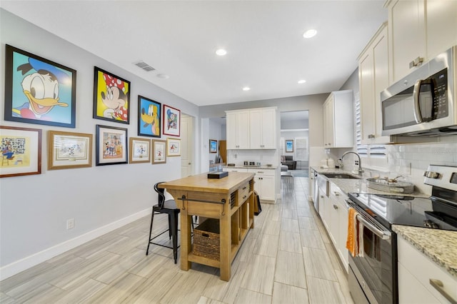 kitchen featuring light stone countertops, decorative backsplash, stainless steel appliances, and white cabinets