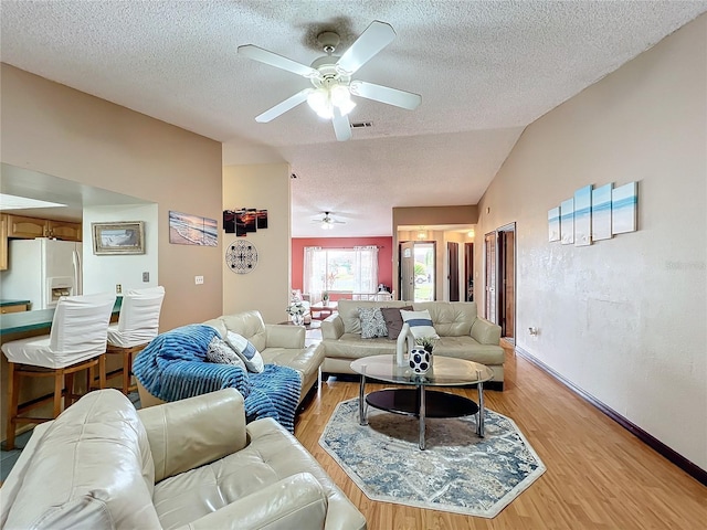 living room with ceiling fan, lofted ceiling, a textured ceiling, and light wood-type flooring