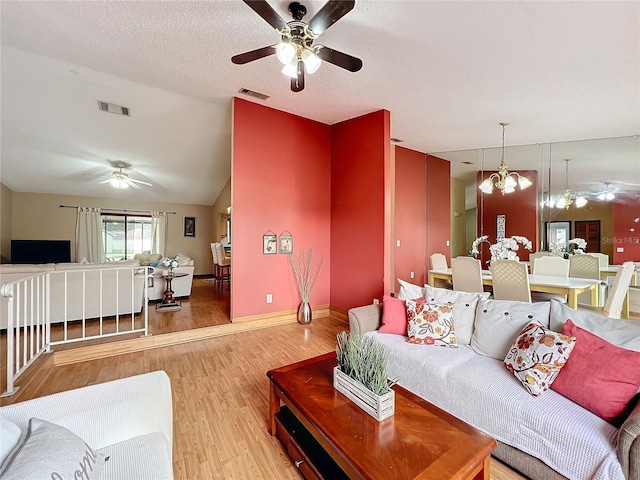 living room featuring lofted ceiling, ceiling fan with notable chandelier, light hardwood / wood-style floors, and a textured ceiling