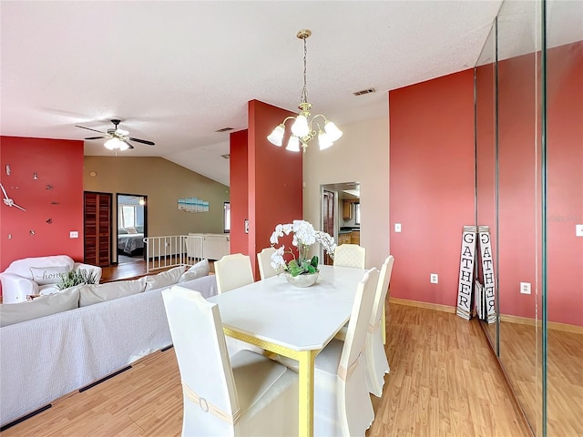 dining space with vaulted ceiling, ceiling fan with notable chandelier, and light hardwood / wood-style floors