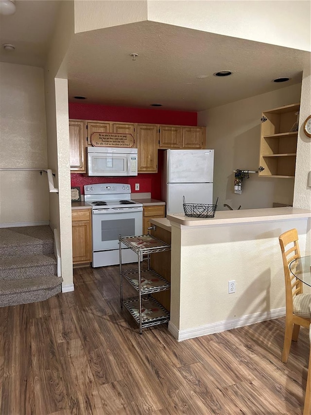 kitchen with dark wood-type flooring, white appliances, and kitchen peninsula