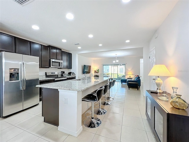 kitchen with sink, stainless steel appliances, a kitchen breakfast bar, light stone countertops, and a center island with sink