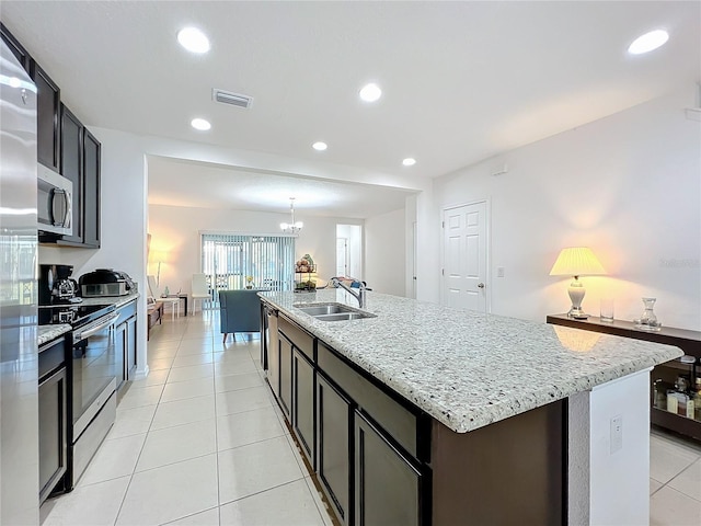 kitchen with appliances with stainless steel finishes, an island with sink, sink, light tile patterned floors, and light stone countertops